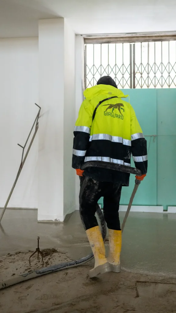 Operaio edile durante la posa di massetto autolivellante in un cantiere di grandi dimensioni