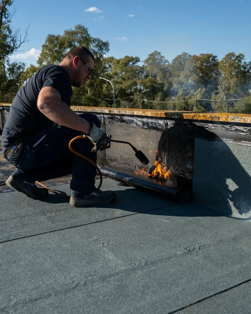 Operaio edile impegnato nella posa di guaina impermeabilizzante sul tetto di un edificio commerciale