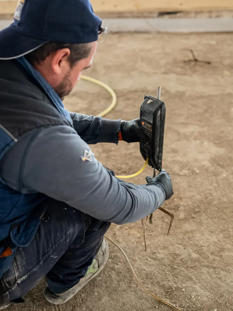 Operaio edile impegnato in rilevazioni sul cantiere per prevenire problemi nella posa del massetto
